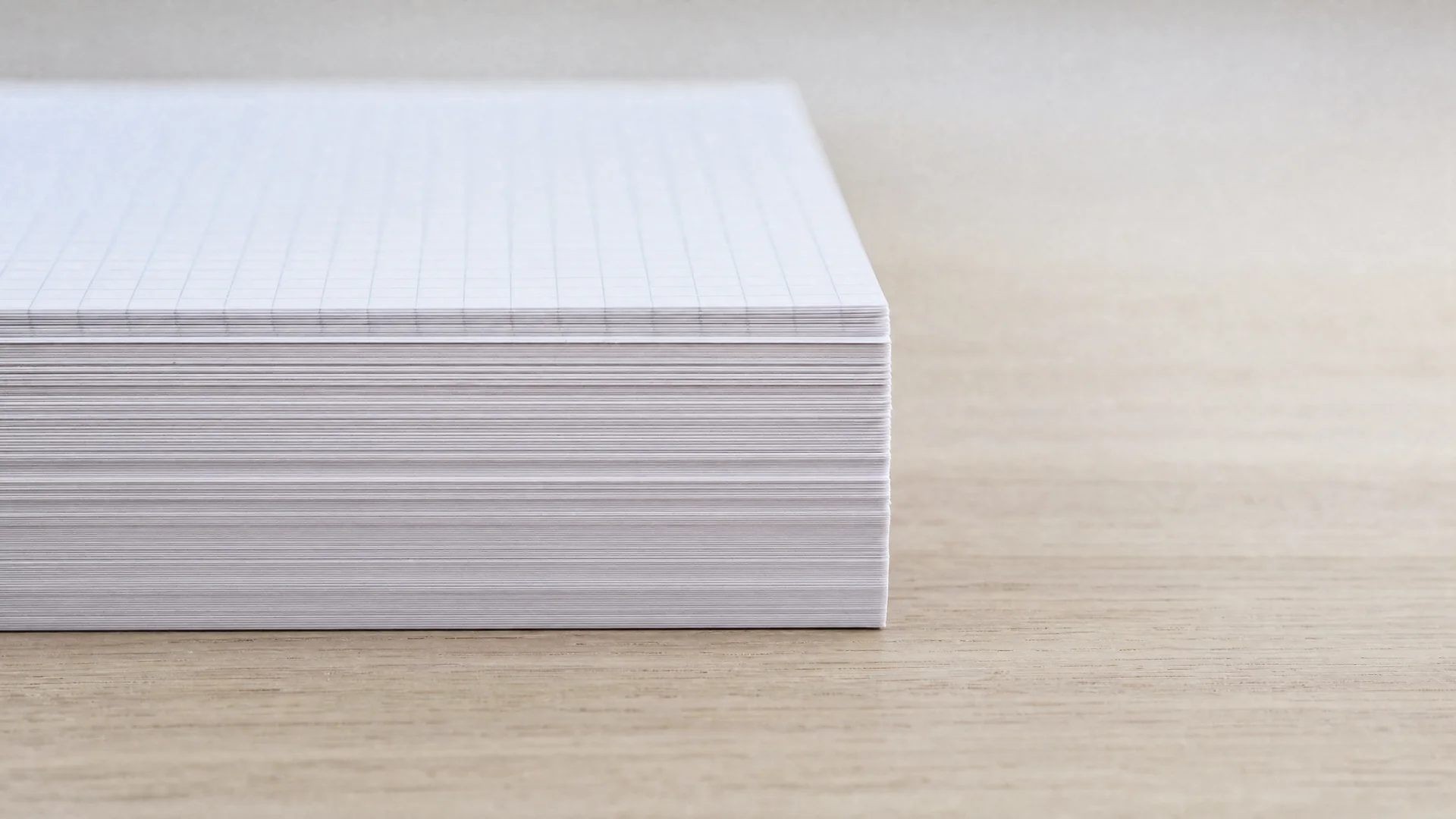 A stack of squared exercise paper photographed edge-on, the layered sheets forming fine horizontal strata.